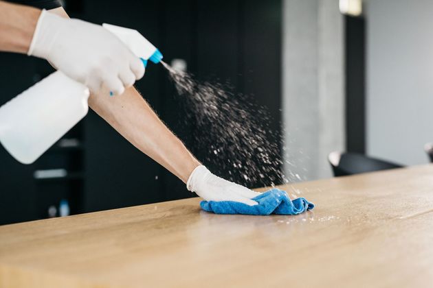 A person is cleaning a wooden table with a spray bottle and a cloth.