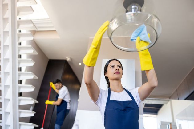 A woman in yellow gloves is cleaning a light fixture in a room.