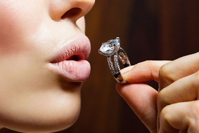 Person holding a diamond ring near parted lips in a close-up shot