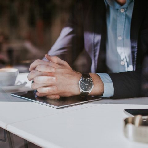 Person in a suit with clasped hands wearing a wristwatch