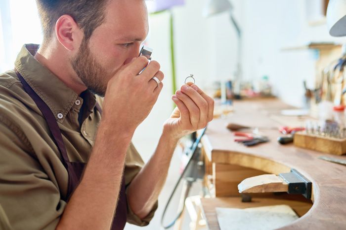 Jeweler examining a ring with a loupe at a workbench in a bright studio