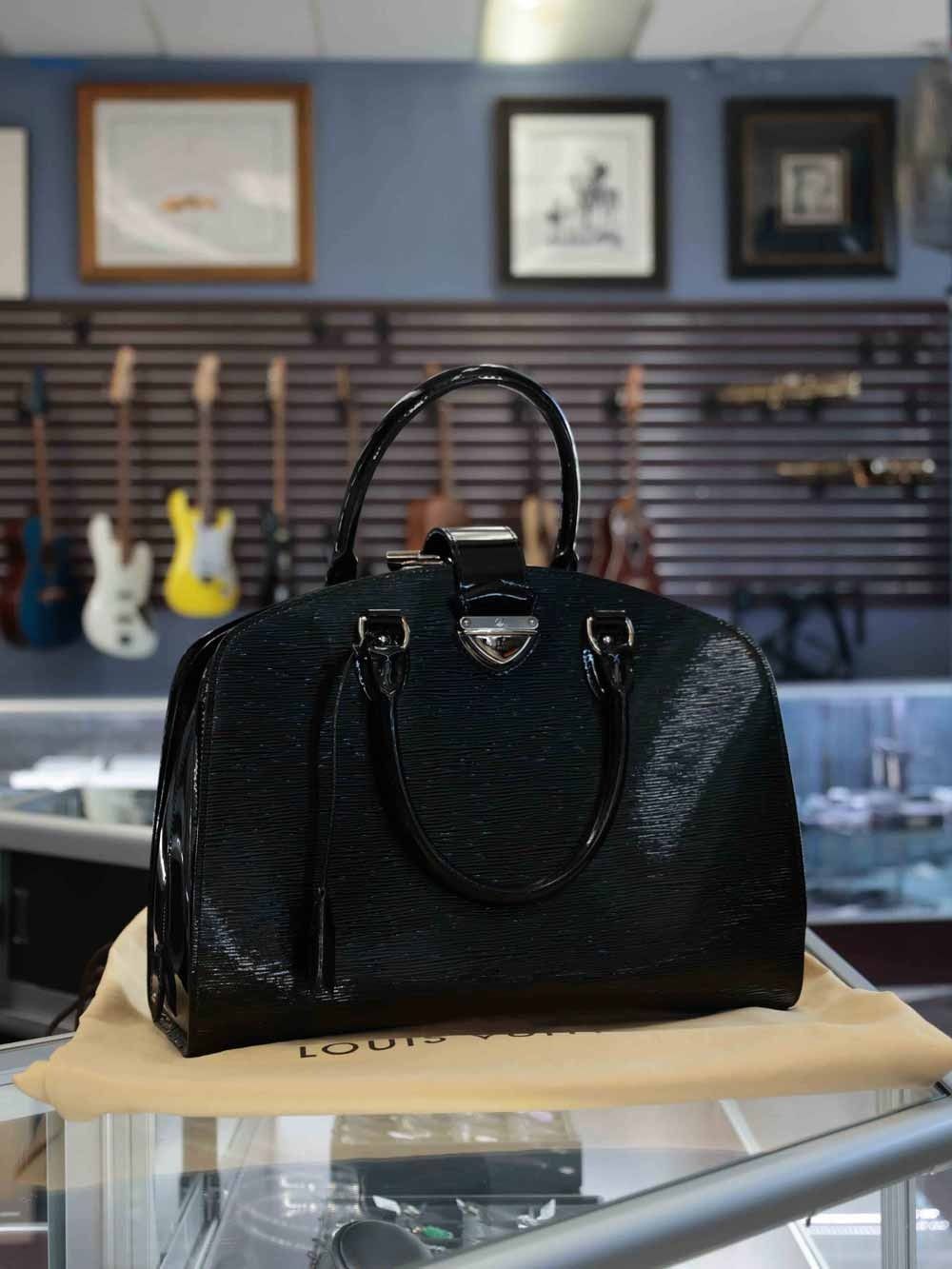 Black leather handbag on display in a boutique with guitars and framed art in the background