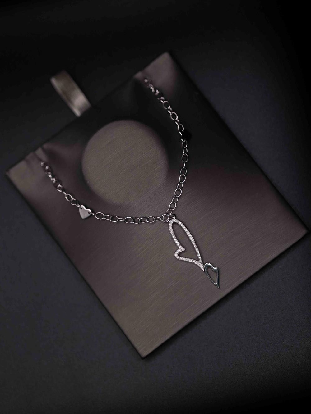 Silver heart pendant necklace on a black display card.