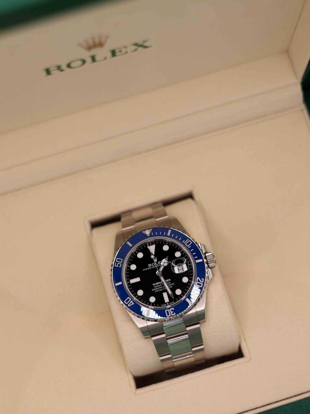 Rolex watch in an open presentation box, silver band with blue bezel and black face.
