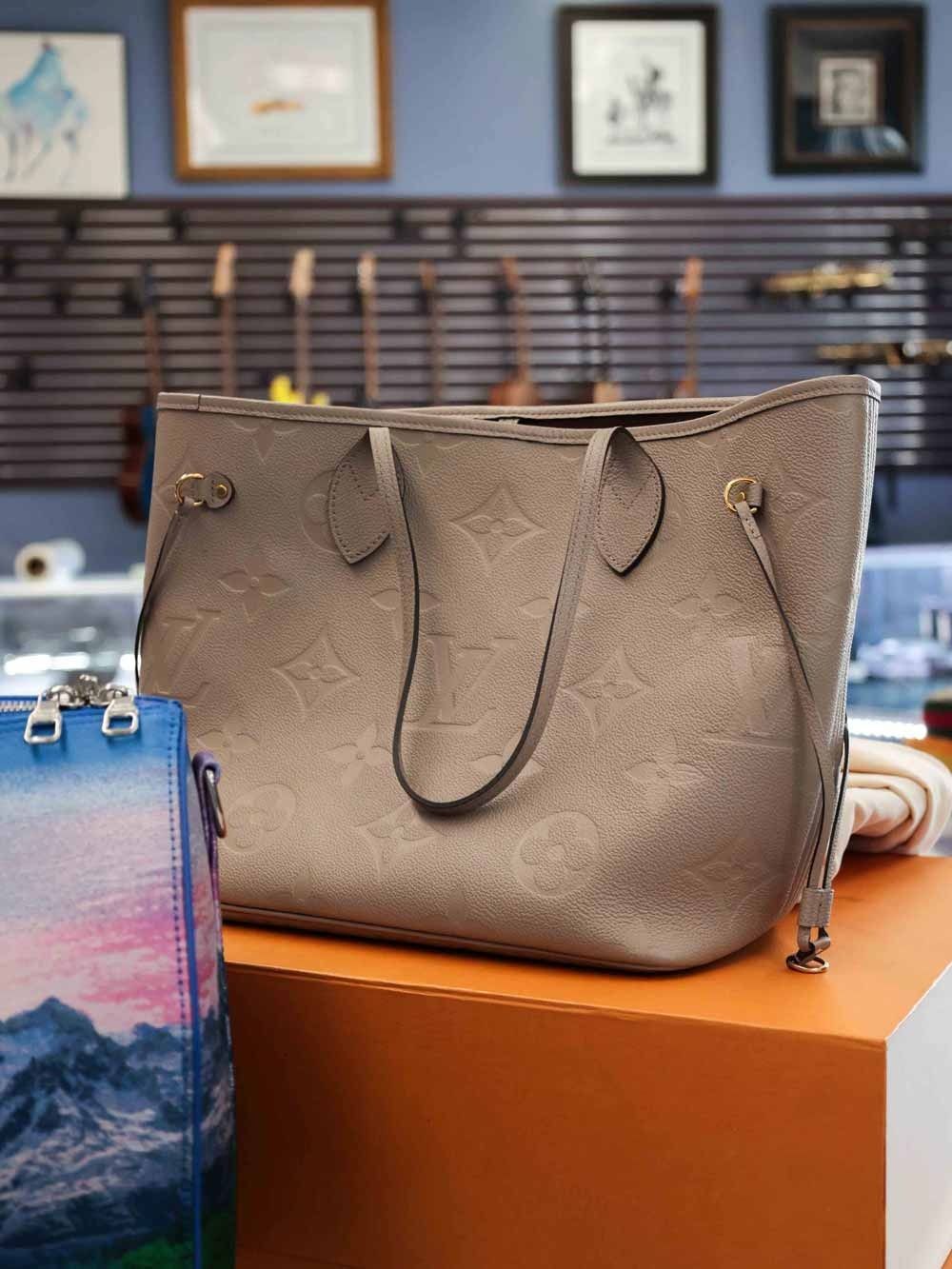 Gray tote bag on an orange display block in a shop, with framed wall art and hanging items in the background