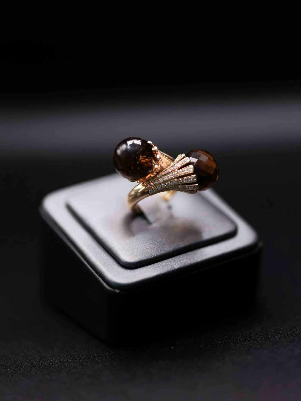 Gold-and-black decorative ring displayed on a black jewelry stand against a dark background