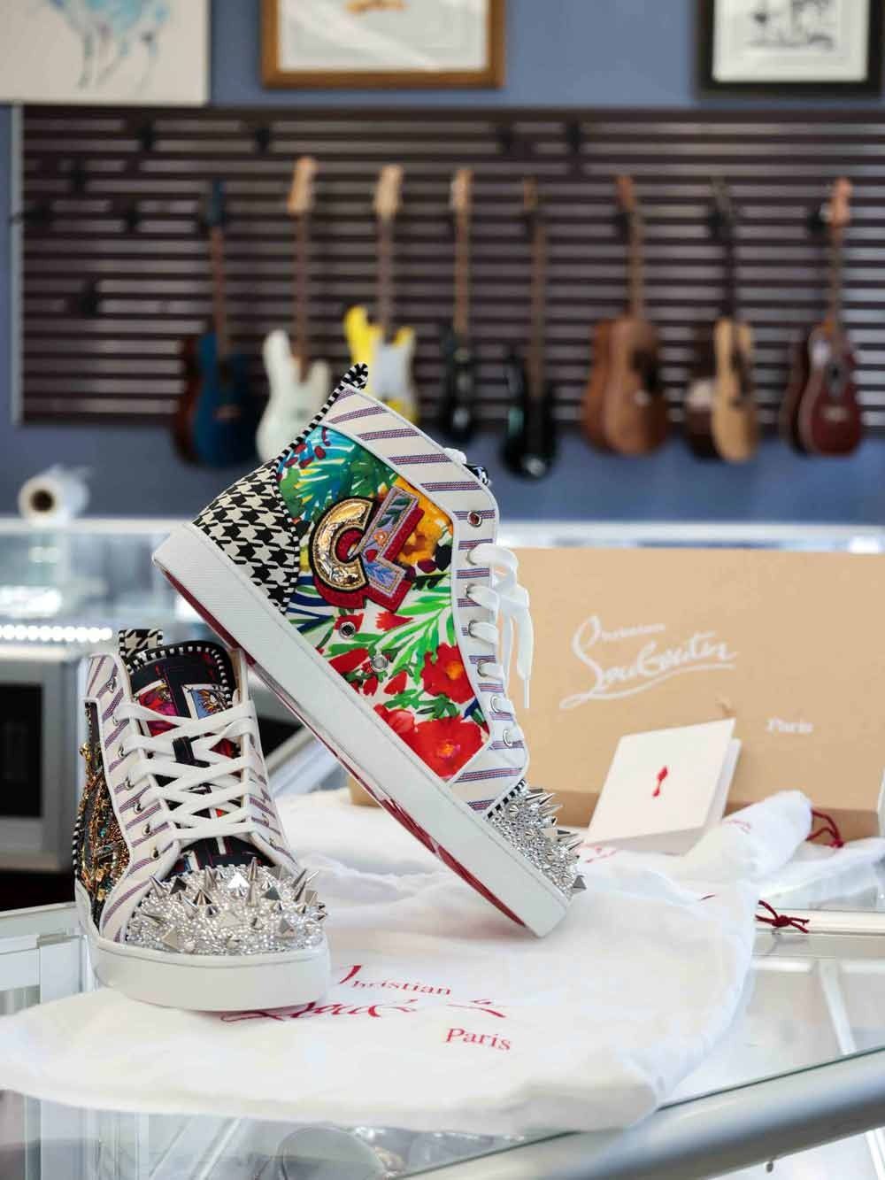 Custom illustrated high-top sneakers on a table in a shoe store workshop, with guitars on the wall behind them