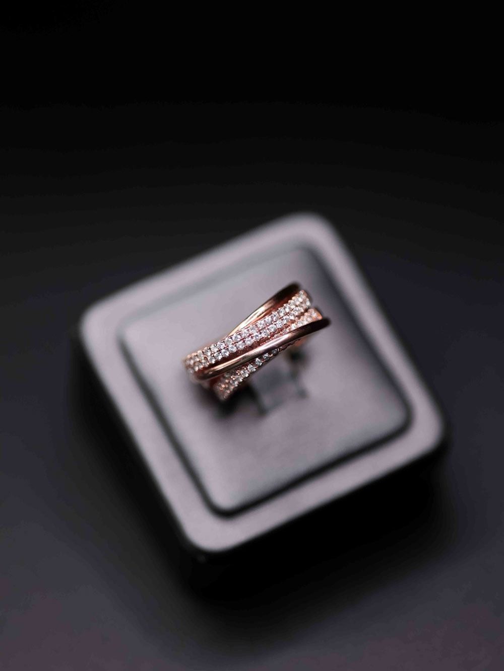 Rose gold ring with pave diamonds on a gray display cushion against a dark background