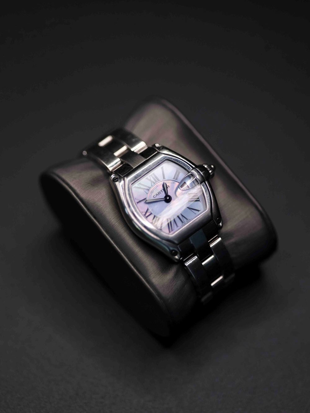 Silver wristwatch on a black display cushion against a dark background.