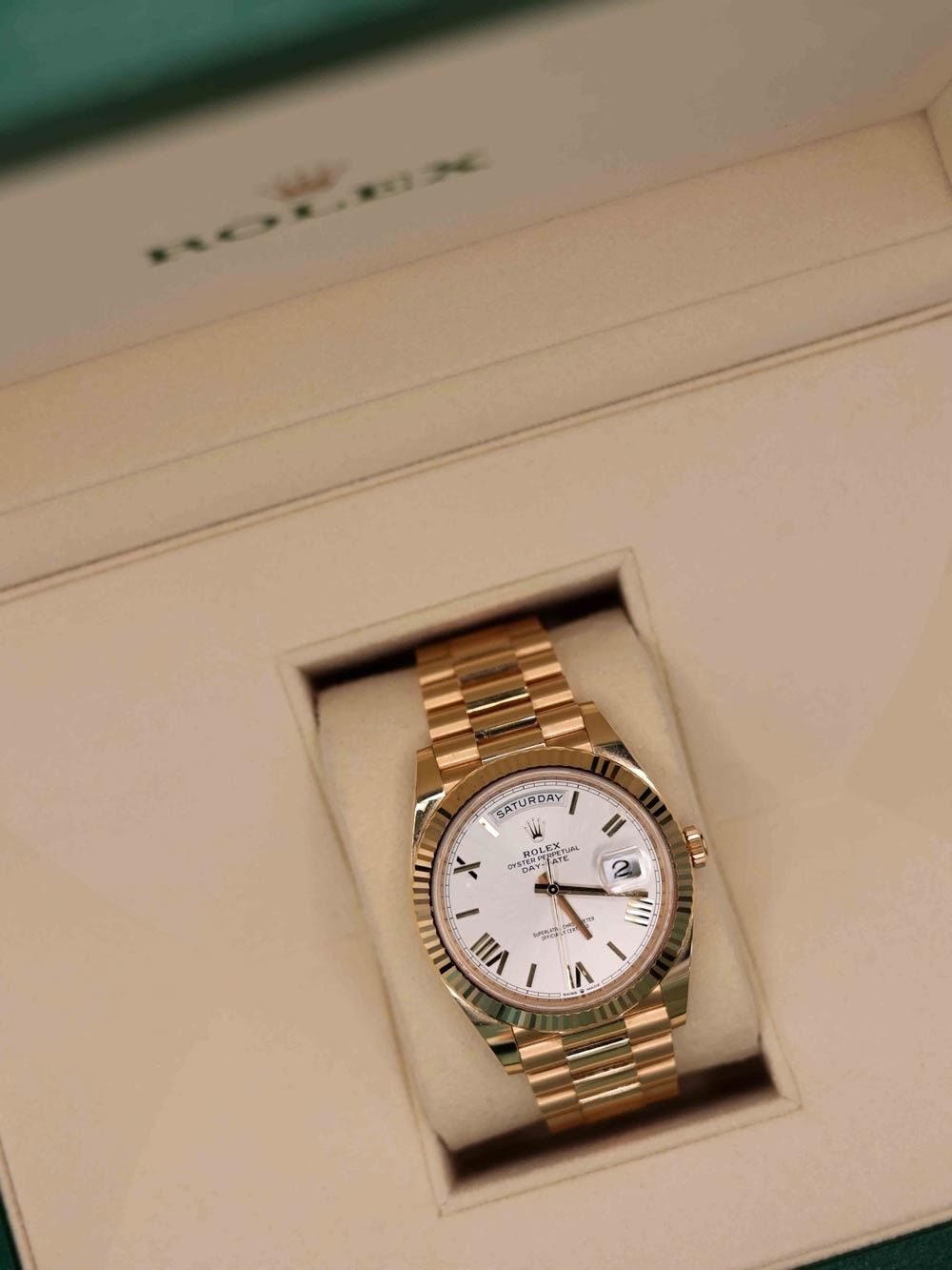Gold wristwatch with white dial displayed in a cream-colored box.