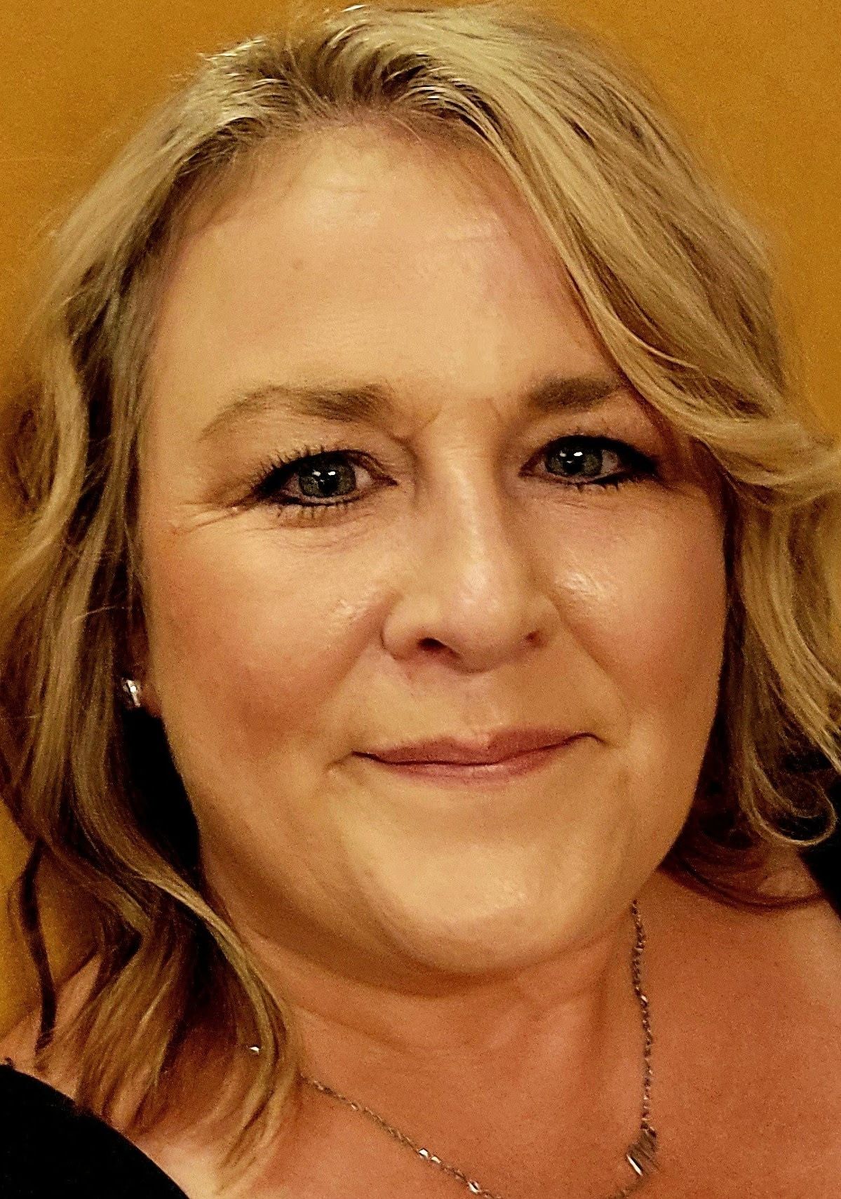 Close-up portrait of a smiling woman with blonde hair in a black top against a warm background
