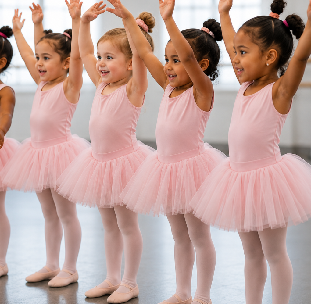 Four young ballet dancers in pink tutus pose with arms raised in a studio.