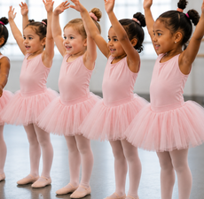 Four young ballet dancers in pink tutus pose with arms raised in a studio.