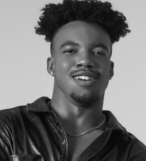 Studio portrait of a smiling person in a black jacket and necklace against a plain background