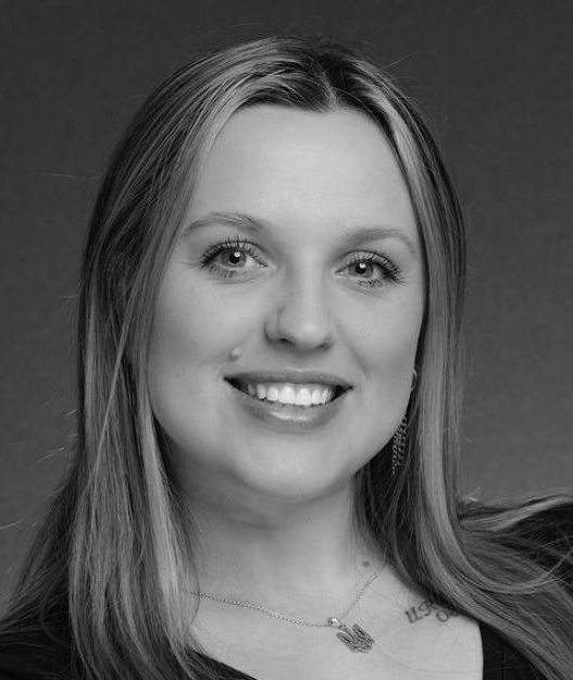 Black-and-white portrait of a smiling woman with long hair and a necklace.