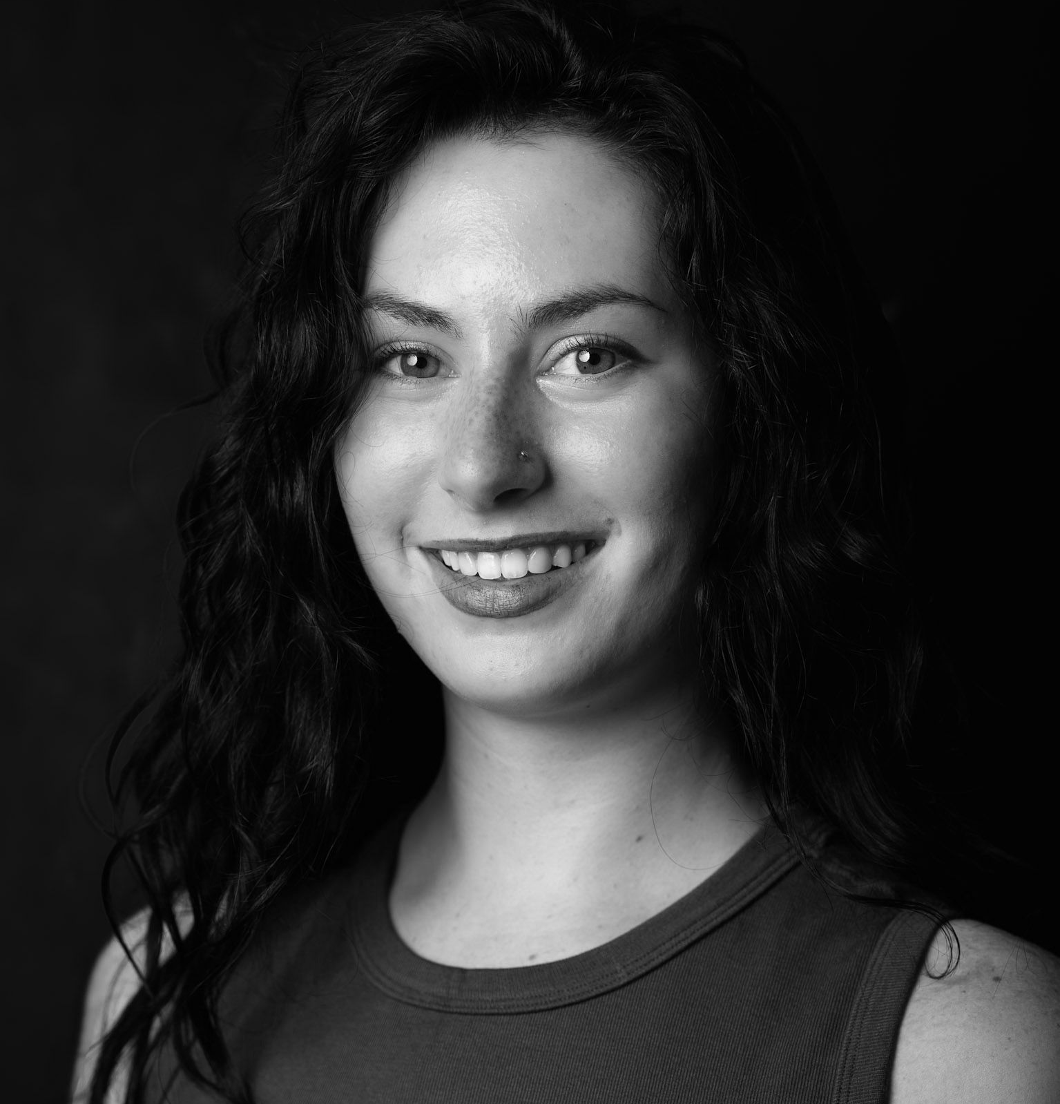 Black-and-white portrait of a smiling person with curly hair against a dark background