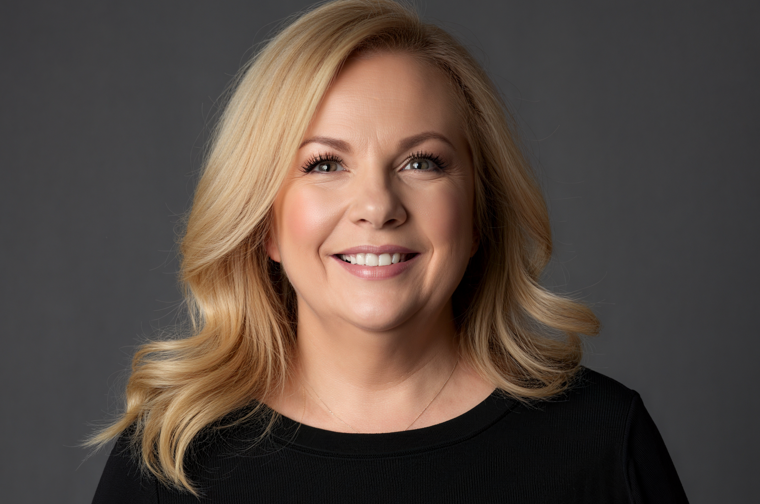 Smiling blonde woman in a black top against a gray background