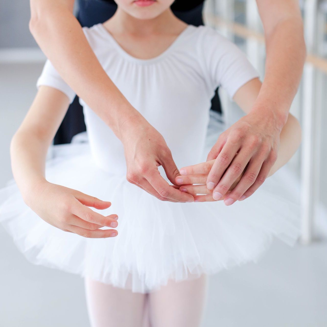 Ballet instructor adjusting a young dancer’s white tutu and arm position in a bright studio