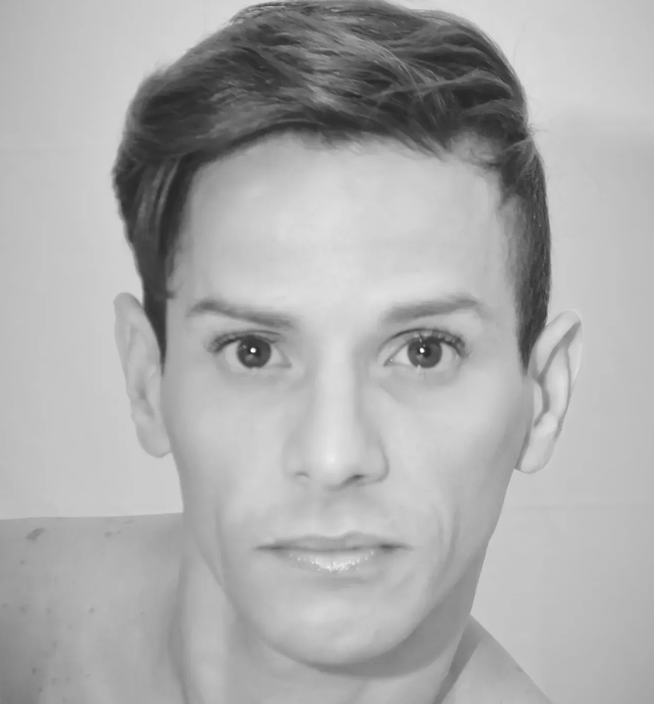 A black-and-white close-up portrait of a person with short hair, looking straight at the camera.