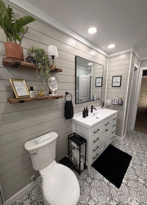 Bright bathroom with white vanity, toilet, black rug, wall shelves, and mirror by a tiled shower