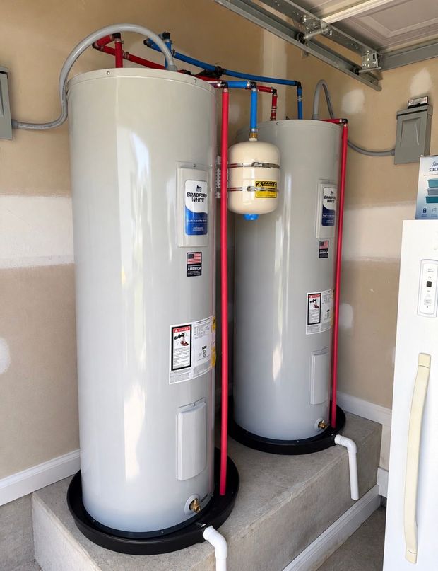 Two tall white water heaters in a utility closet with red and blue pipes and a small tank between them