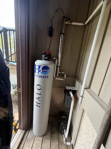 White Ultima water softener tank in a narrow outdoor utility nook beside a house