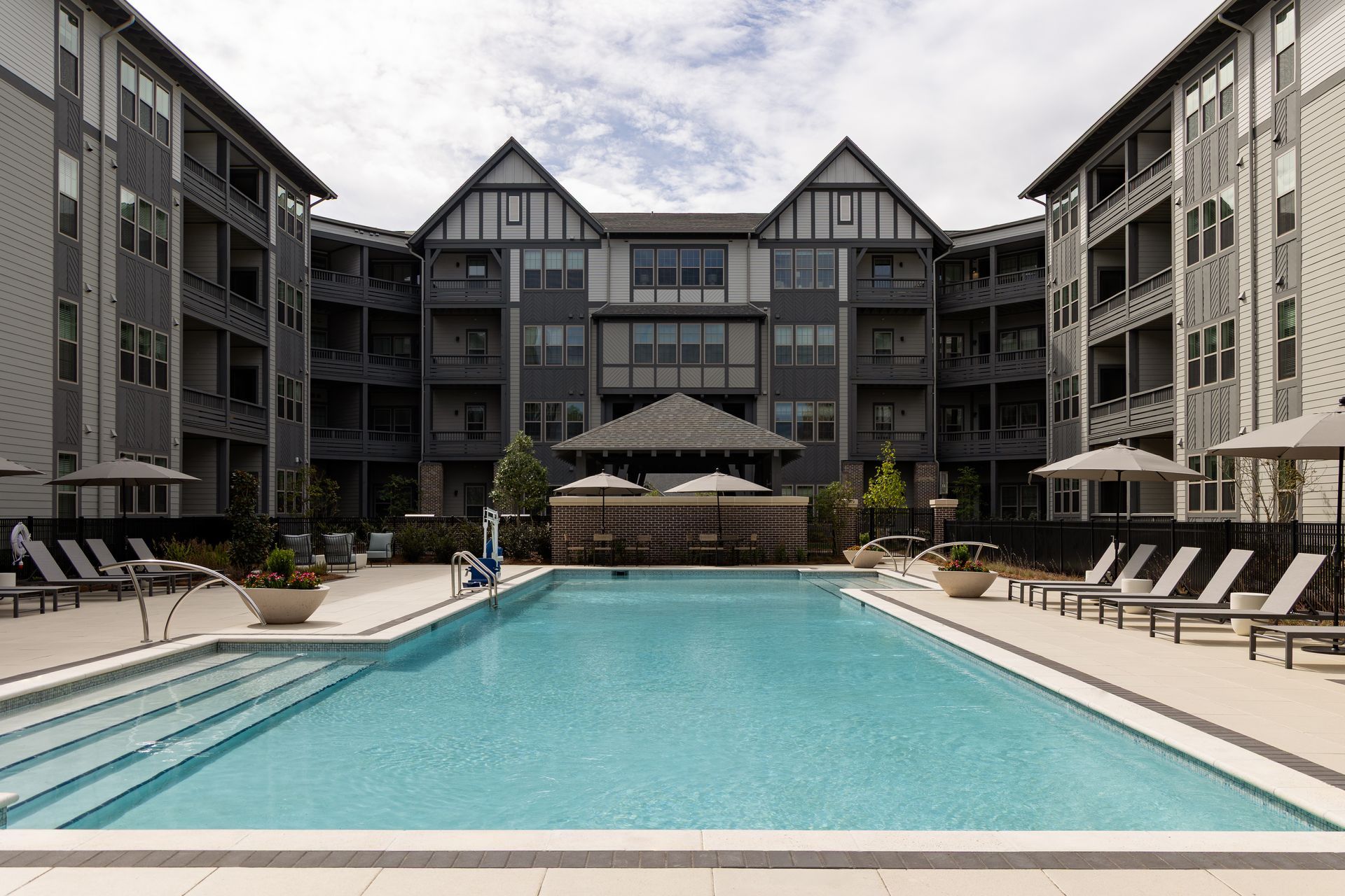 Pool surrounded by apartment buildings with lounge chairs, blue water, and cloudy sky.