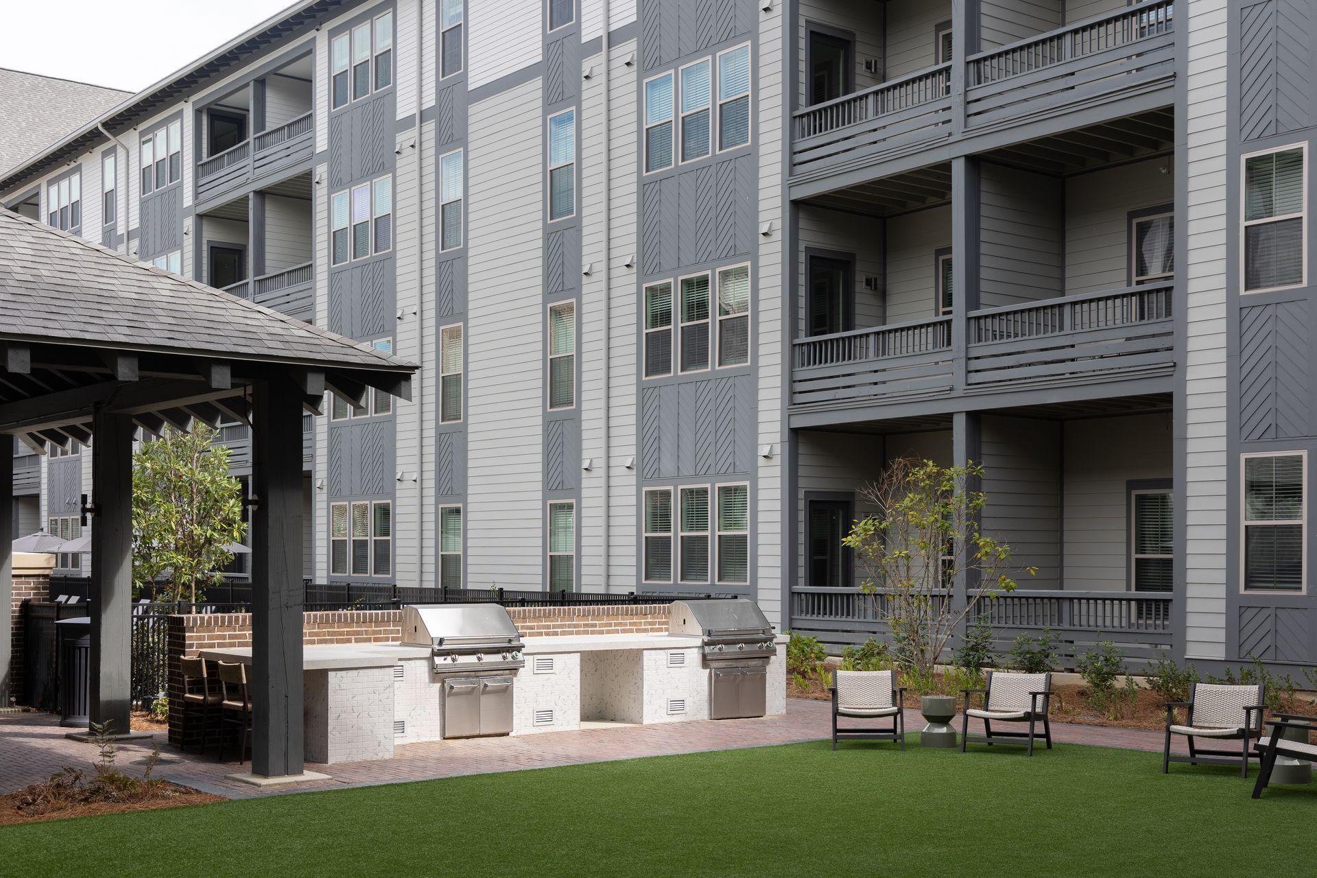 Outdoor grilling area with stainless steel grills and seating in front of a modern apartment building.