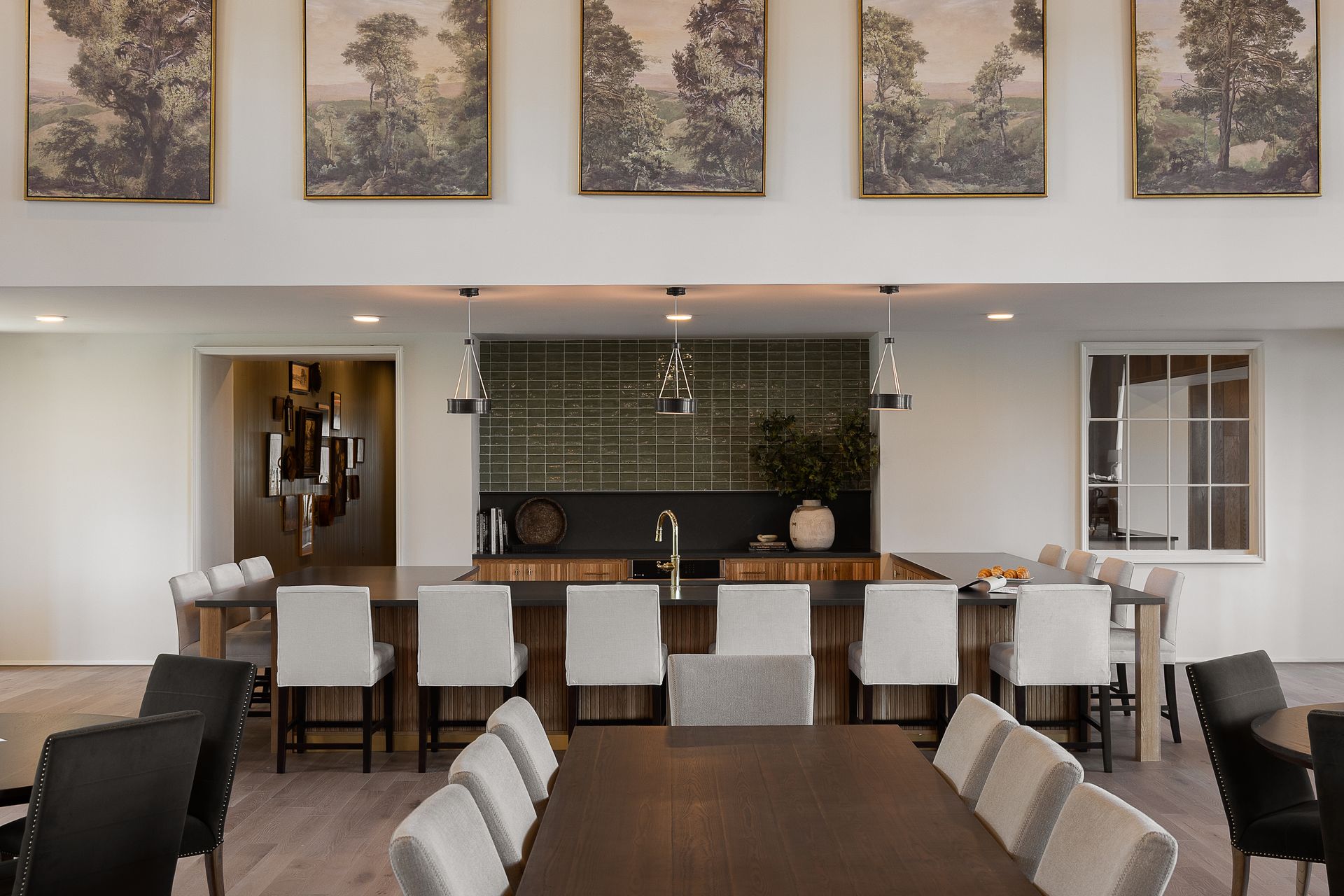 Open-plan resident space with a large island and seating, long dining tables, and landscape artwork.
