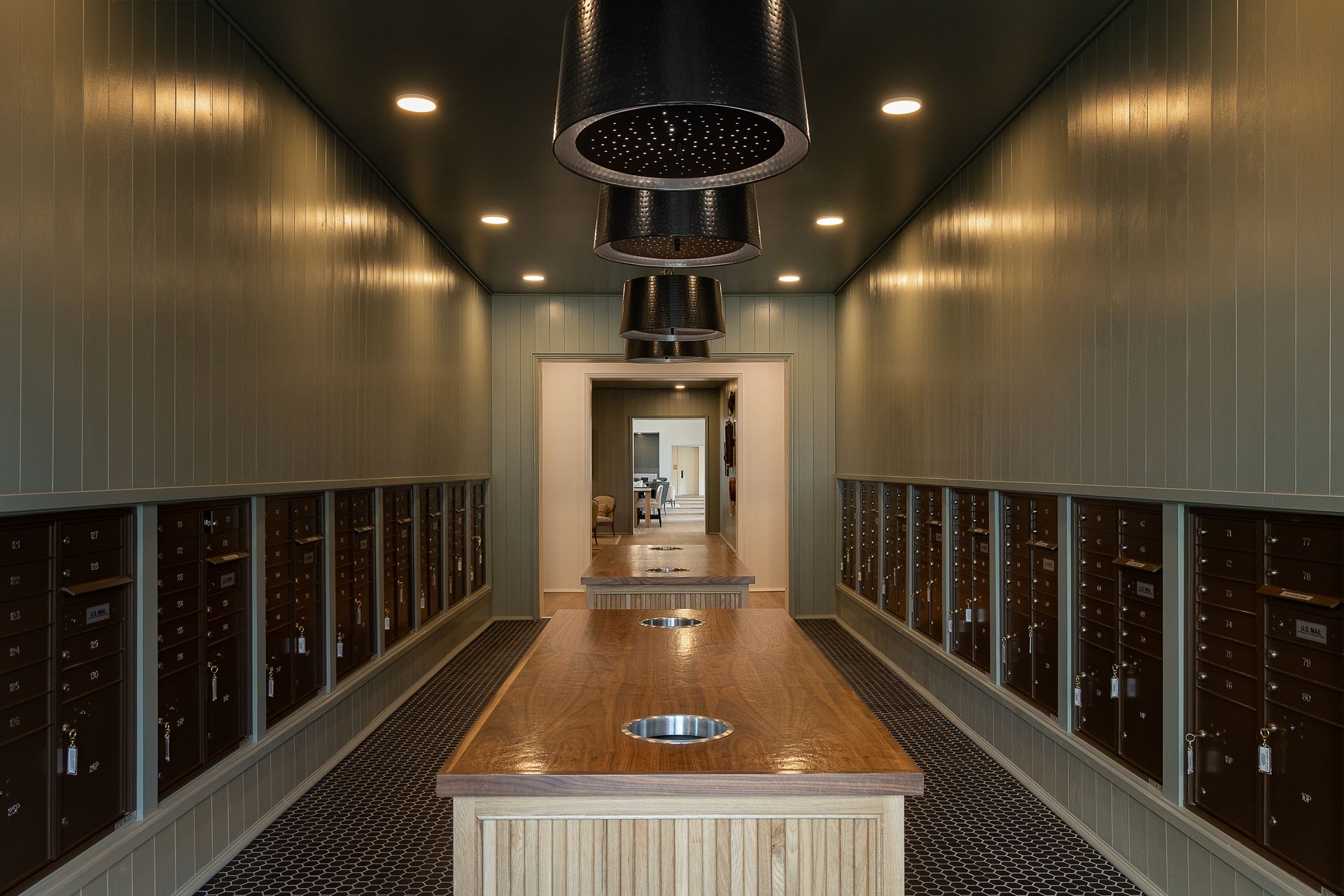 Apartment mailroom with rows of mailboxes. Wooden walls, countertops, and pendant lights.