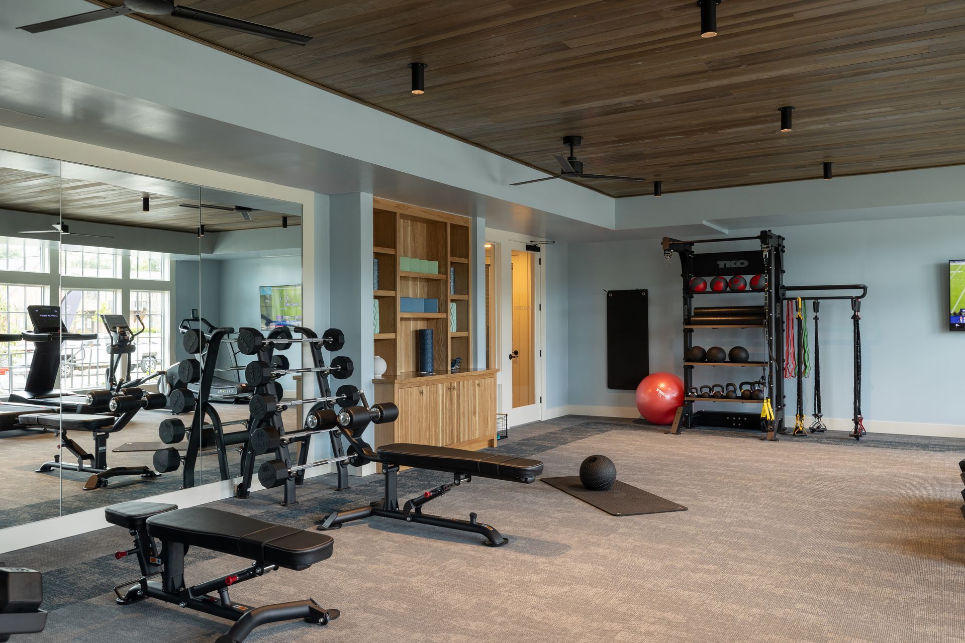 Gym with weights, benches, and exercise equipment. Gray carpet, light blue walls, wooden ceiling.