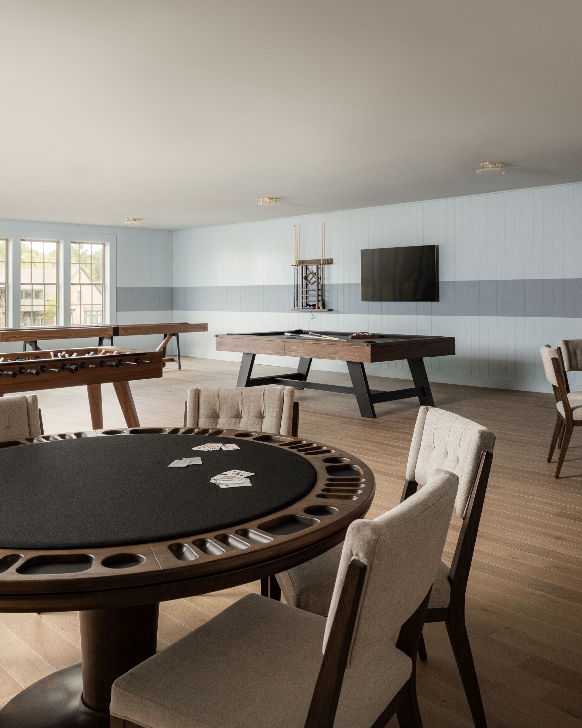 Game room with poker table, pool table, foosball, TV, and light blue and gray wall stripes.