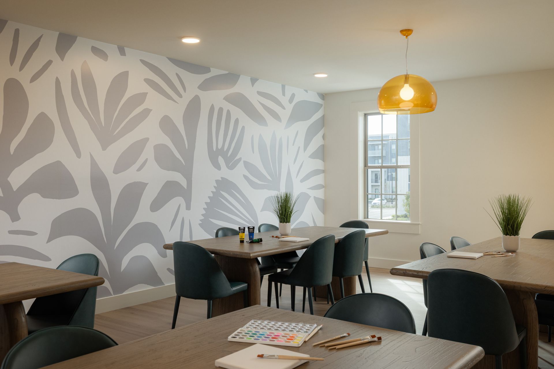 Art room with floral mural, tables, chairs, and window with natural light.