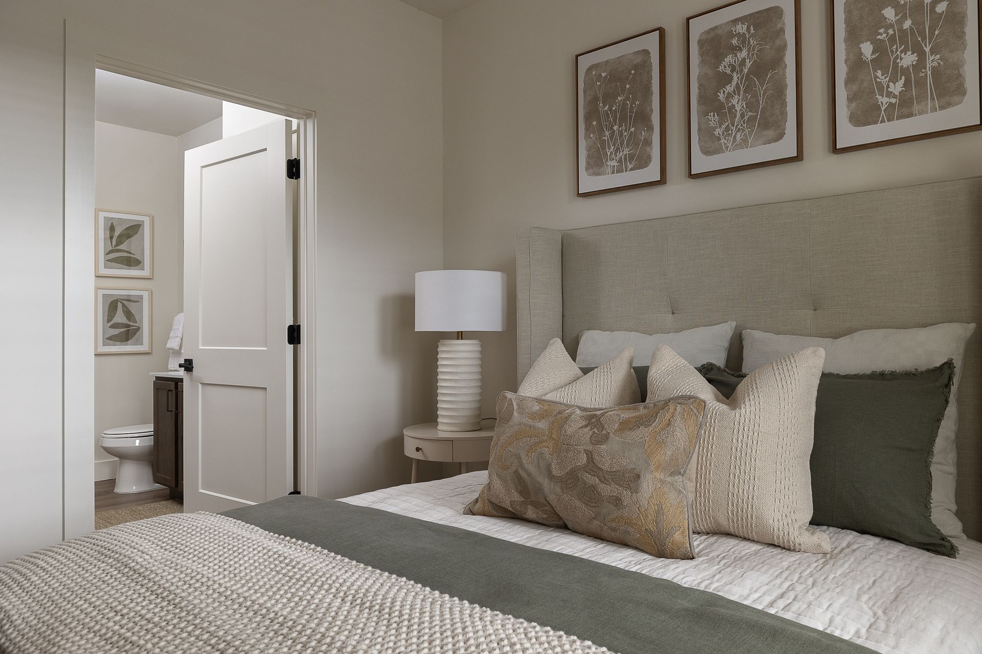Bedroom with bed, neutral colors, and artwork. Open doorway to bathroom visible.