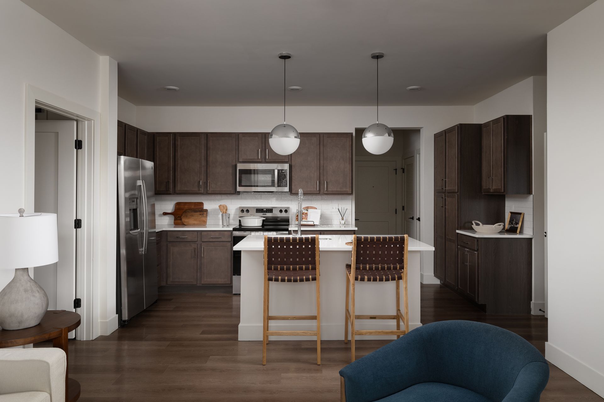 Modern kitchen with dark brown cabinets, stainless steel appliances, and a white island with two bar stools.