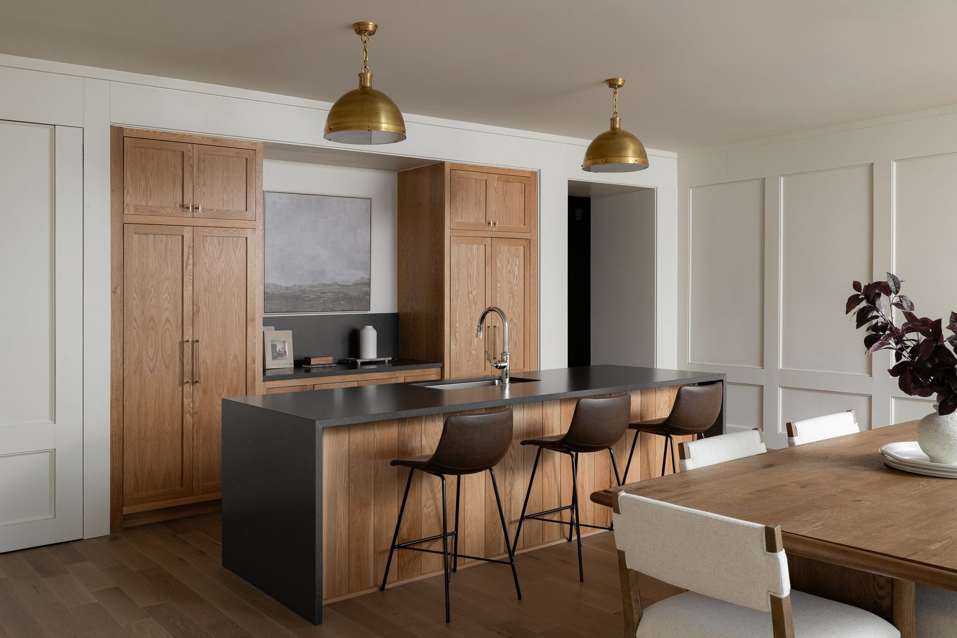 Modern kitchen with wooden cabinets, island with stools, and brass pendant lights.