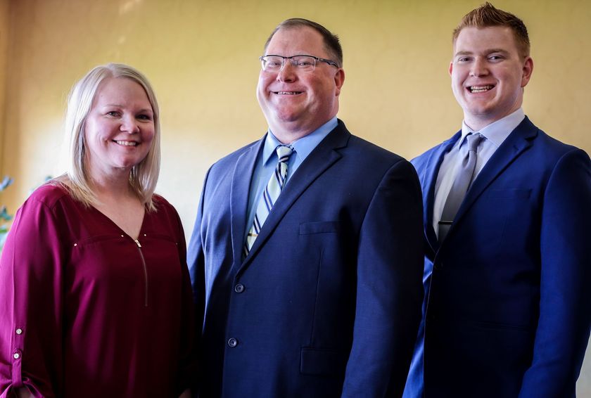 Three people in formal attire posing indoors, smiling at the camera.