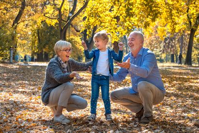 Three people crouch and smile in a sunlit autumn park with golden leaves.