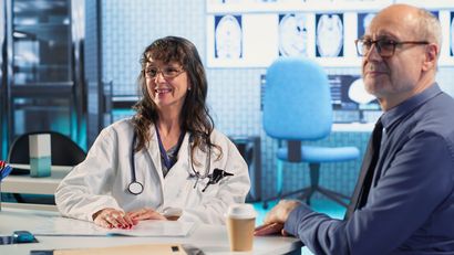 Two people in a medical office reviewing scans, with a stethoscope and coffee cups on the table.