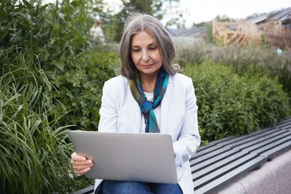 Woman using a laptop on a park bench beside greenery and modern steps