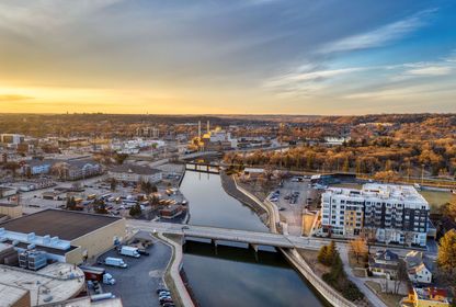 Aerial view of a snowy riverside city at sunset, with bridges, buildings, and warm golden light