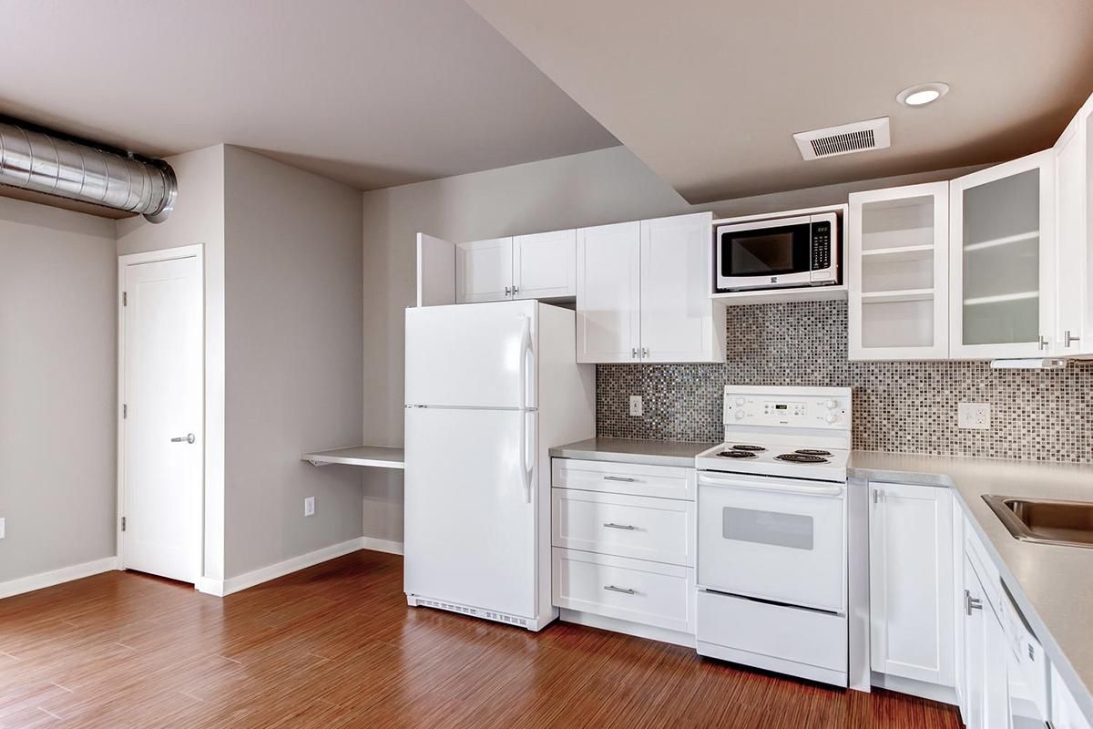White kitchen with appliances, cabinets, and a microwave. Wood floor and a small desk.