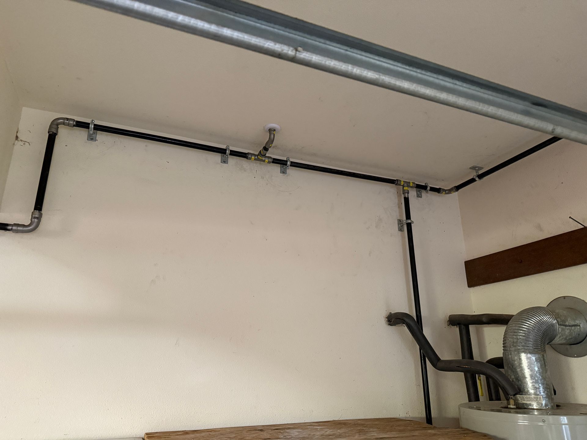 Ceiling corner with exposed metal pipes and a vent in a utility room
