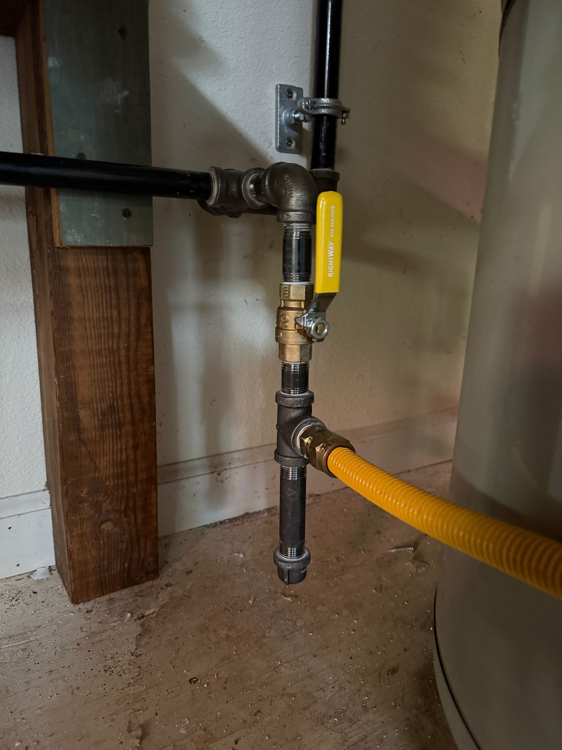 Gas pipe valve with yellow handle connected to a flexible yellow hose near a wall and floor.