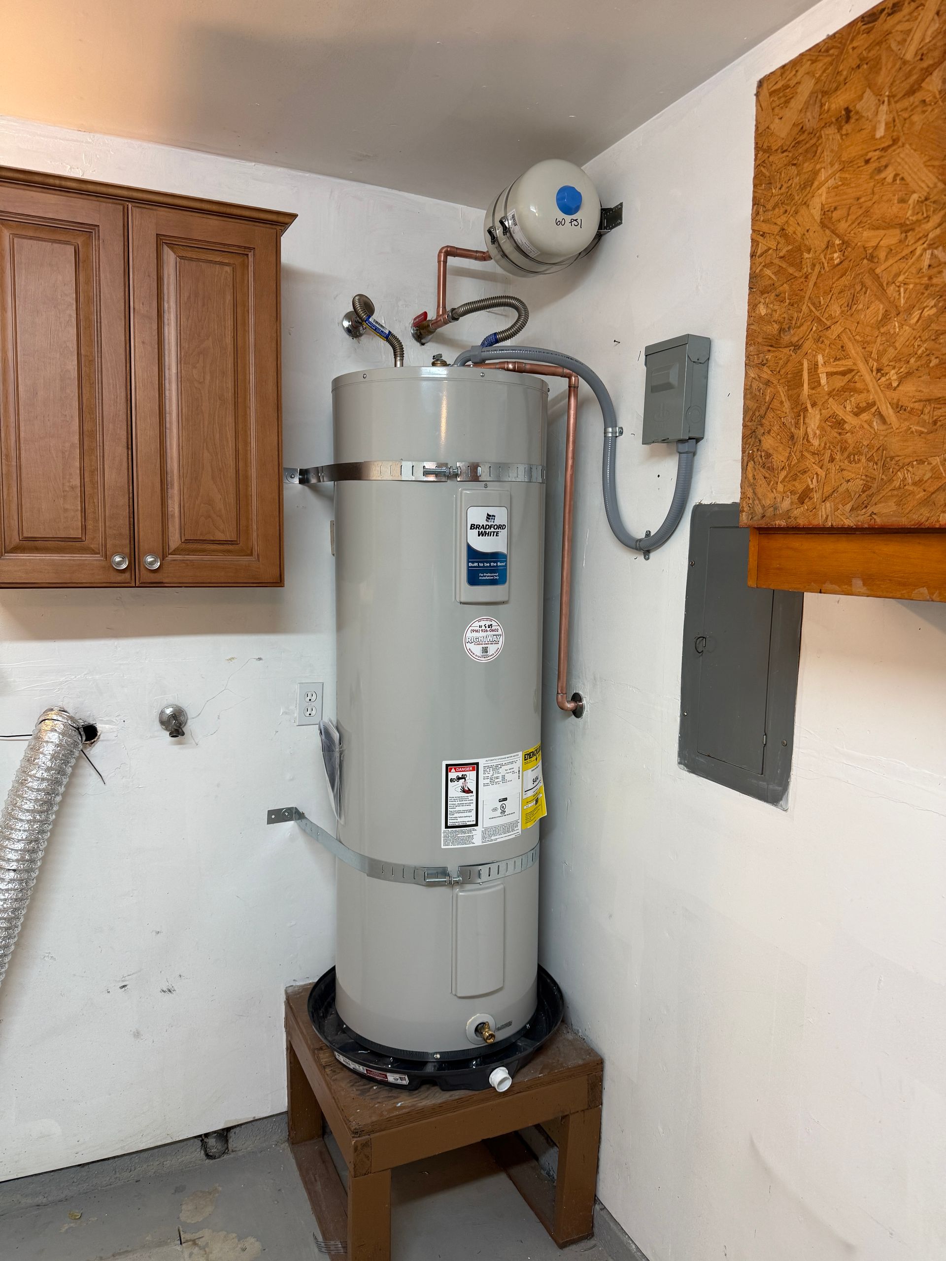 Water heater in a utility room, with copper pipes, an expansion tank, and wooden cabinets.
