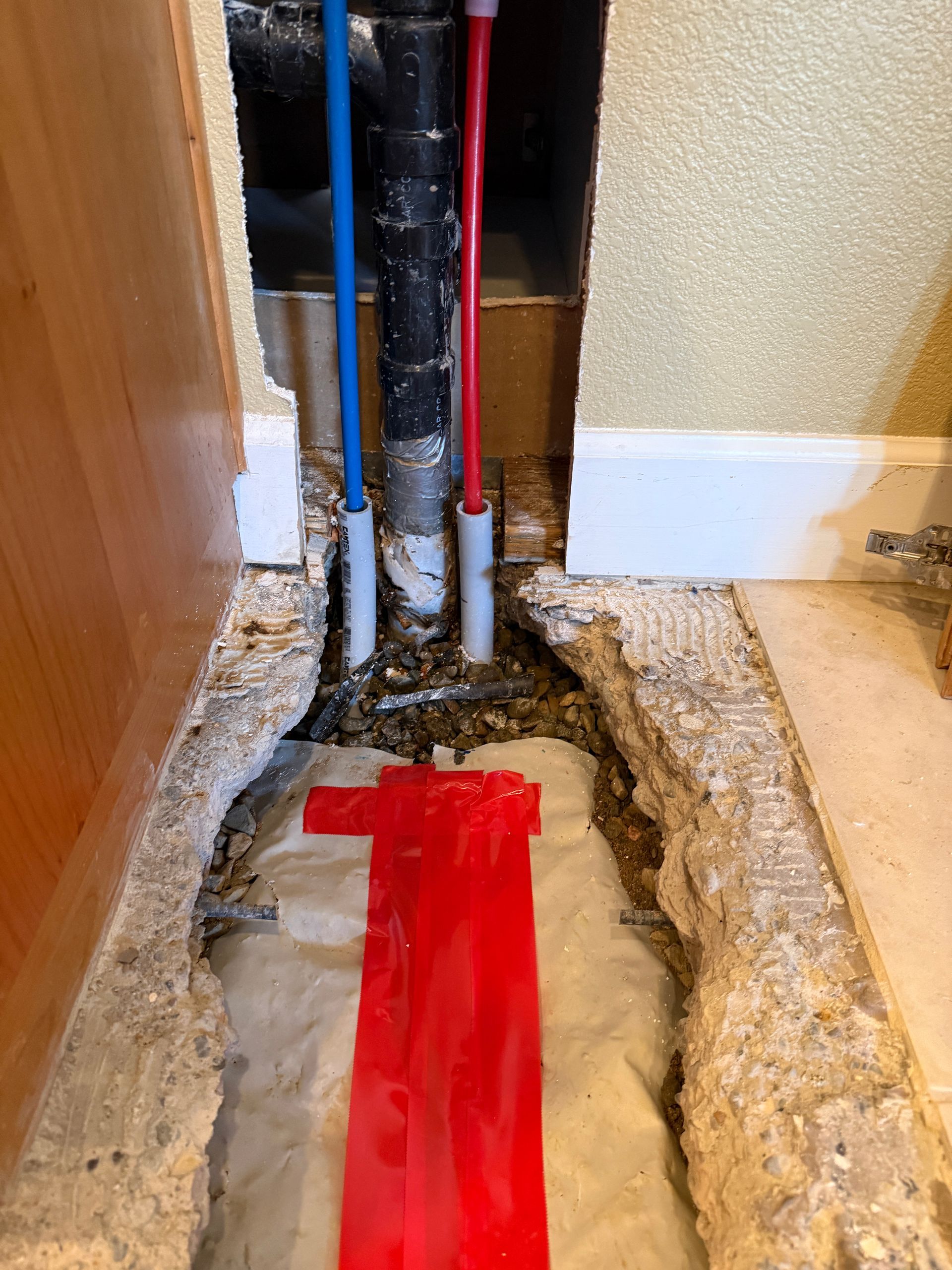 Basement floor repair around red and blue plumbing pipes near a doorway
