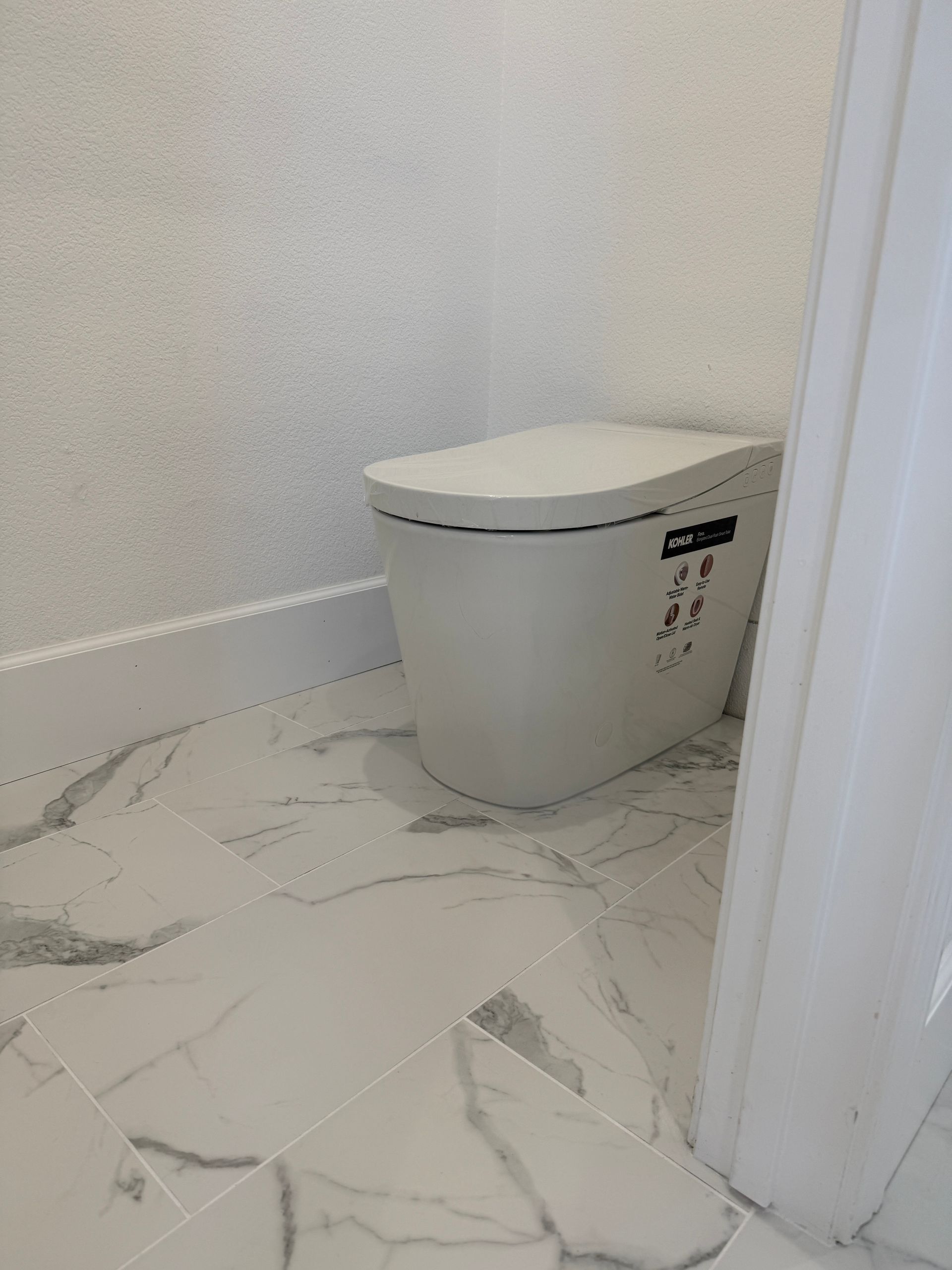 Modern white toilet in a small bathroom with marble-look tile floor and white walls