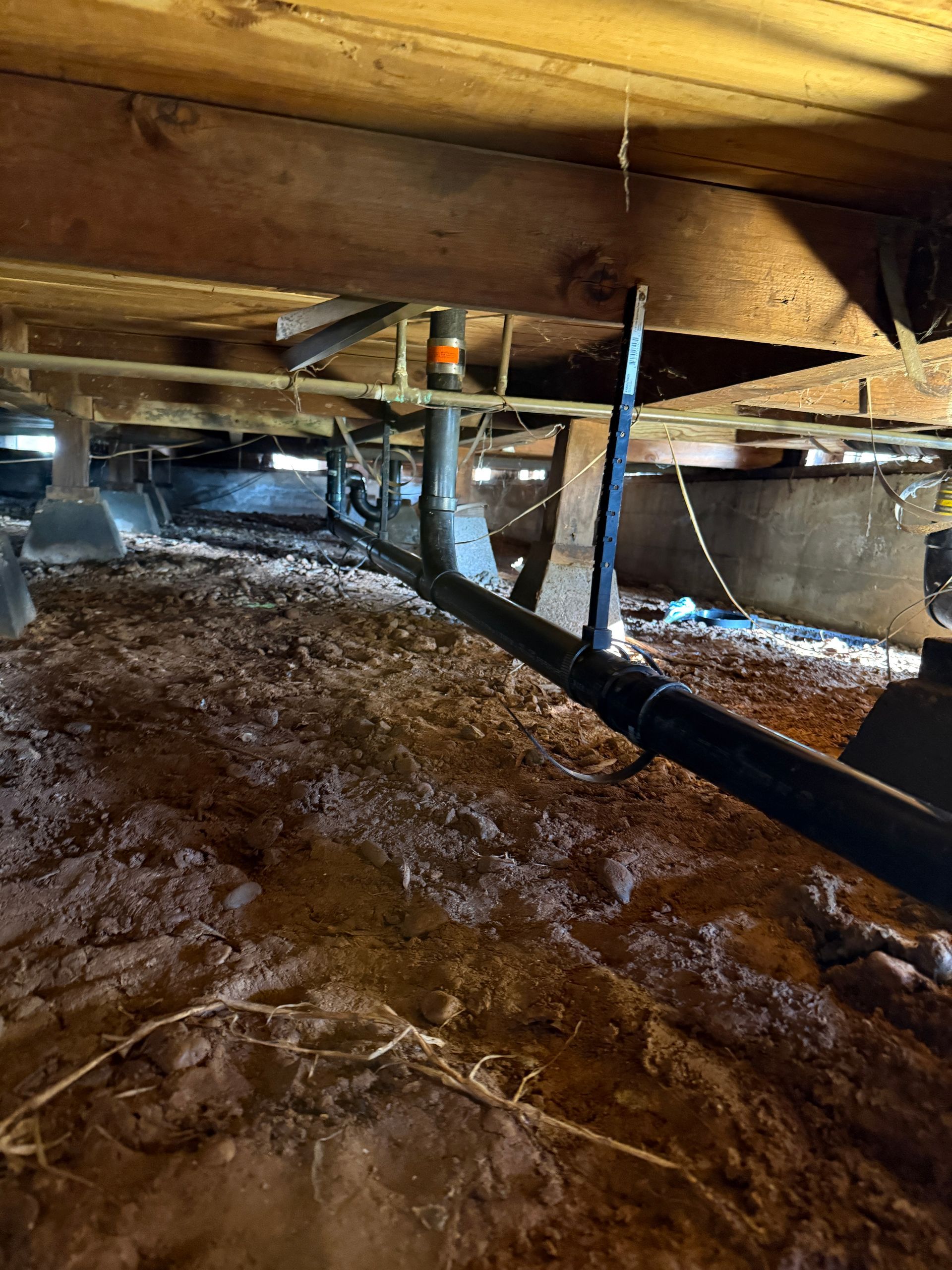 Crawlspace under a house with exposed wooden beams, insulation, ducts, and a dirt floor