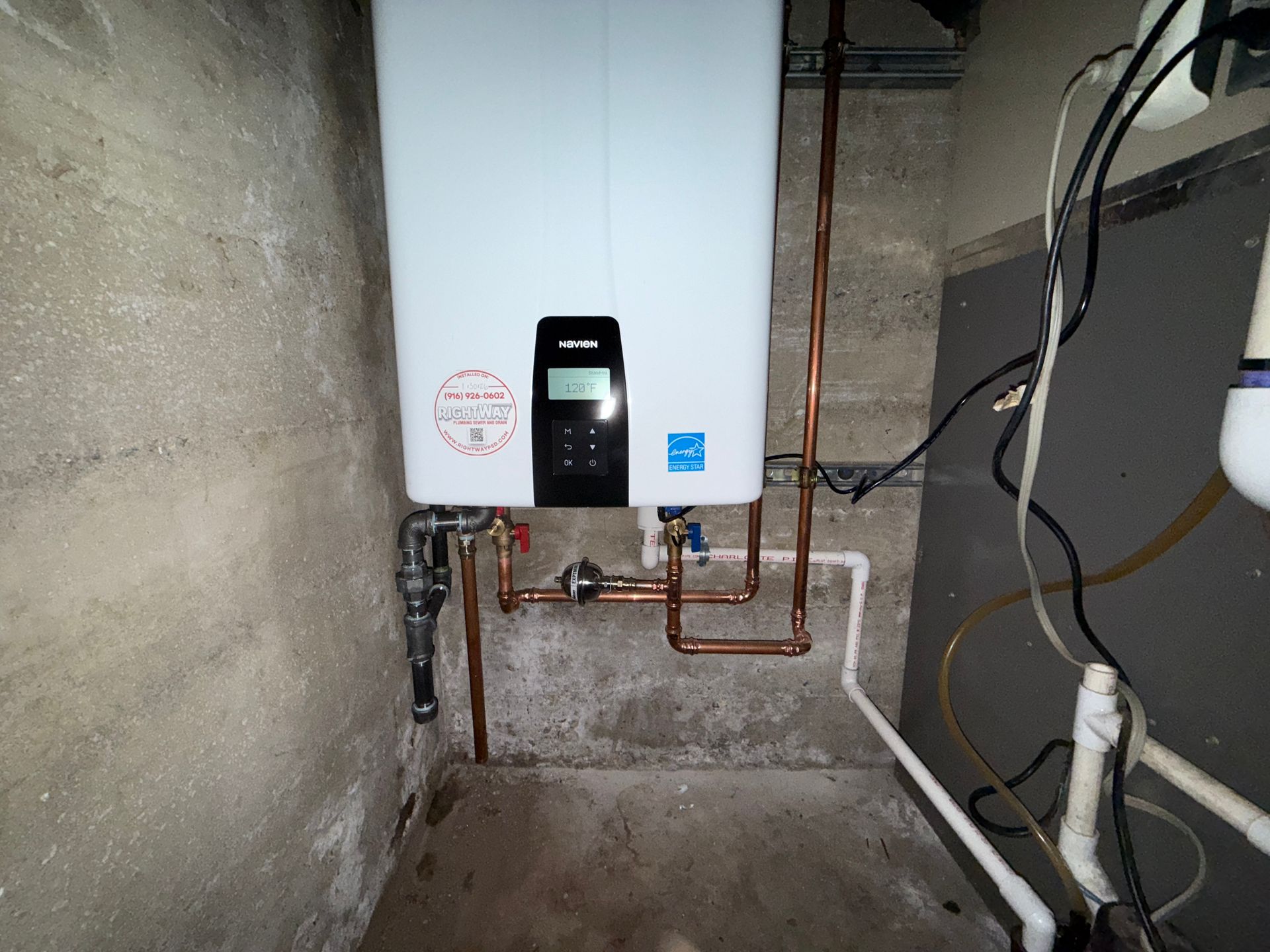 White wall-mounted water heater with copper pipes in a concrete utility room