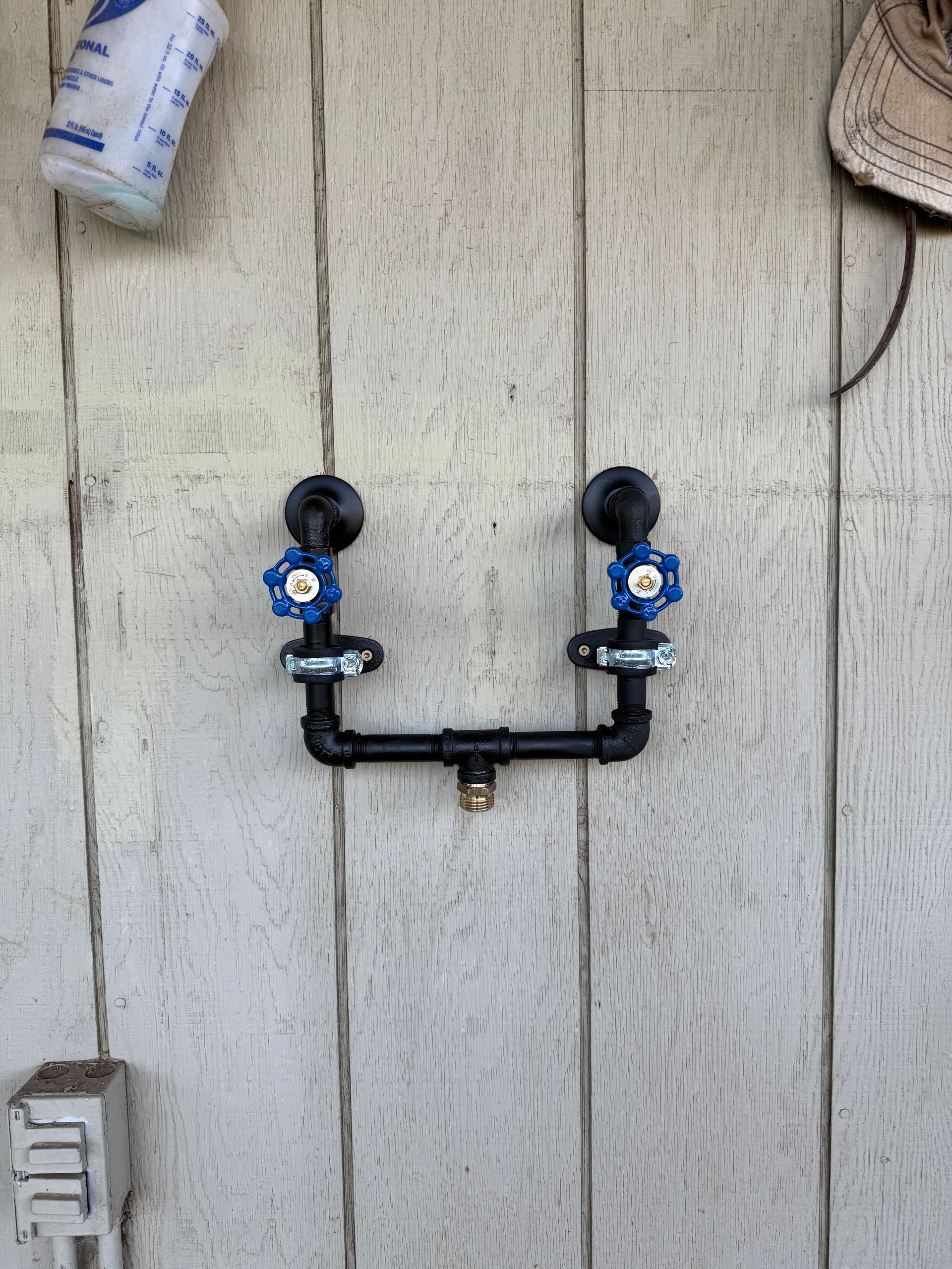 Two blue valves connected by black pipes mounted on weathered wood boards.